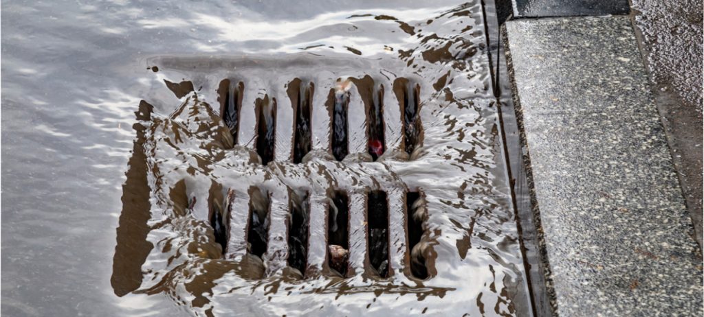 Rainwater flowing into a street drain, illustrating the need for advanced water treatment solutions to reduce pollutants and improve water quality.