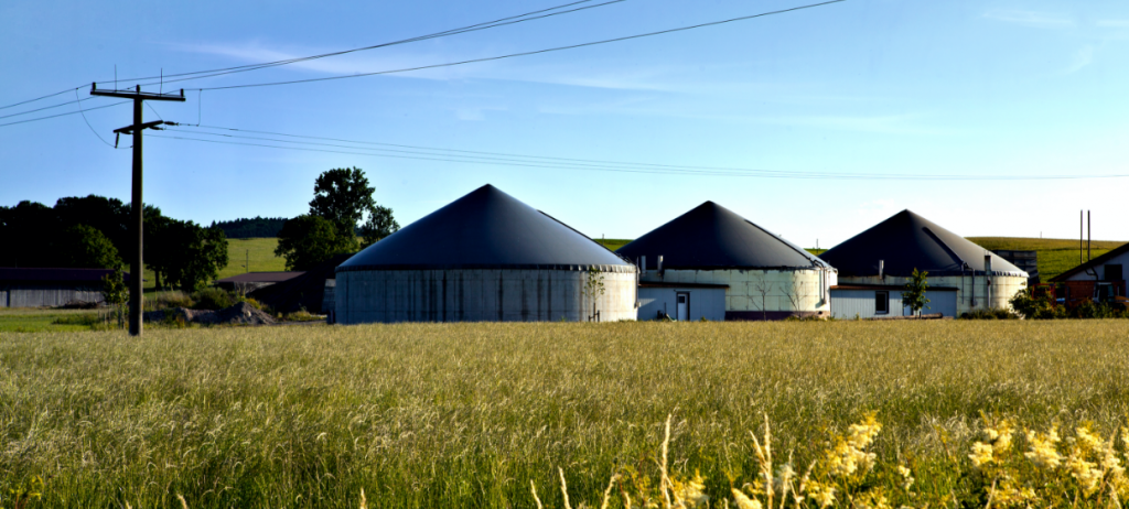 Image of biogas plants surrounded by a grassy field under a clear blue sky, representing renewable energy production and sustainable environmental practices." These details highlight the renewable energy aspect and sustainability focus associated with biogas facilities